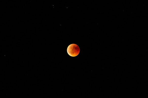Horizontal long shot of an orange and red moon in the dark sky at night